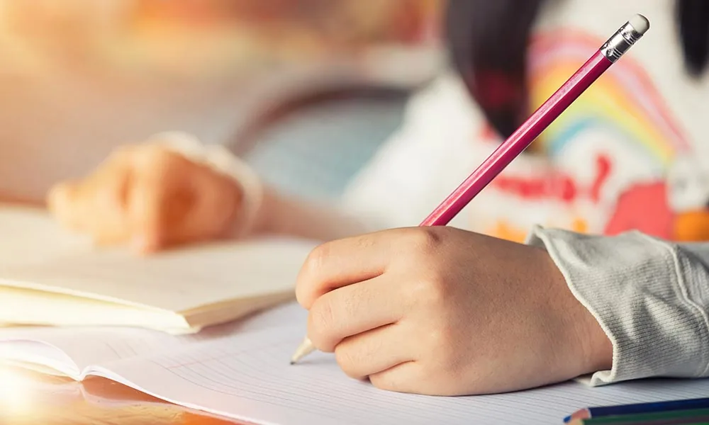 Main d'enfant écrivant au crayon dans un cahier