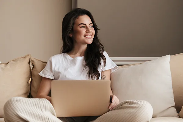 Jeune femme souriante réservant en ligne depuis son canapé